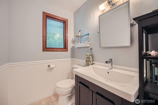 half bath featuring tile patterned floors, vanity, toilet, and wainscoting