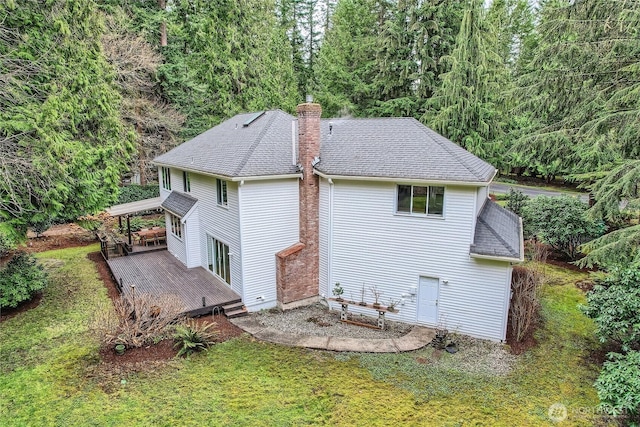 back of property with a lawn, a chimney, a deck, and roof with shingles