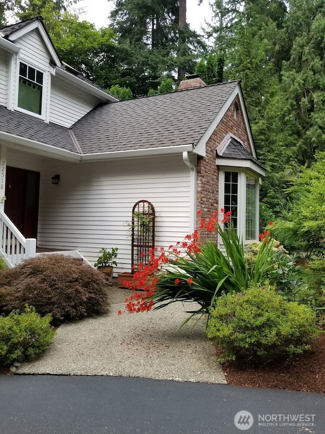 view of property exterior with brick siding, a chimney, and roof with shingles