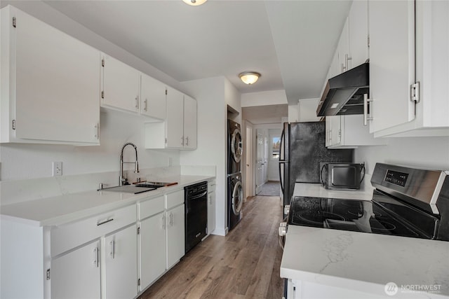 kitchen with stacked washing maching and dryer, stainless steel electric stove, a sink, black dishwasher, and under cabinet range hood