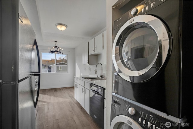 clothes washing area featuring light wood finished floors, stacked washer / dryer, a chandelier, laundry area, and a sink