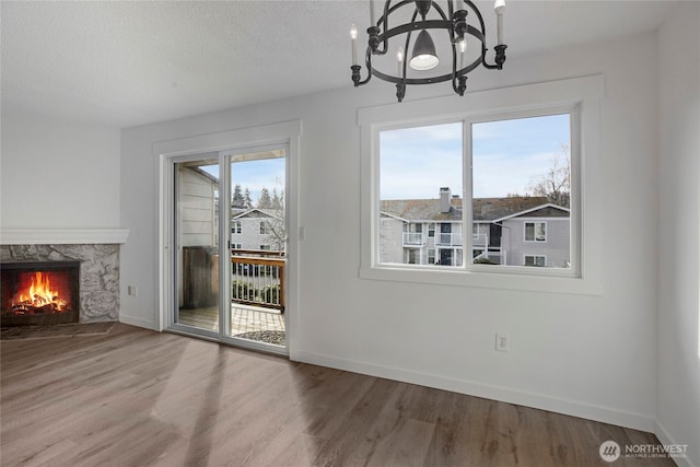 unfurnished dining area featuring a high end fireplace, baseboards, wood finished floors, a notable chandelier, and a textured ceiling