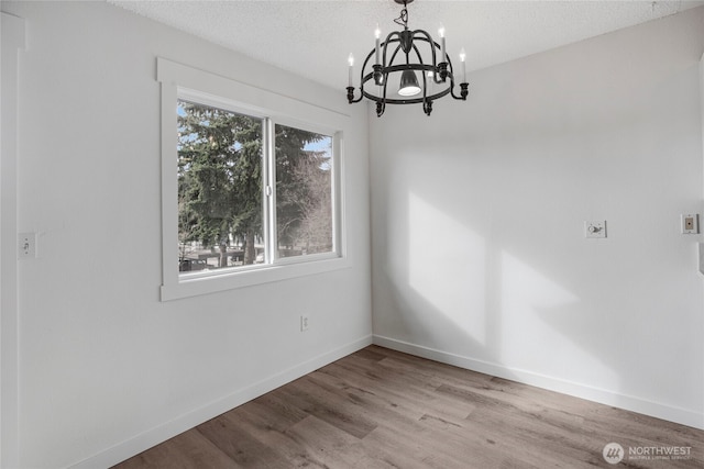 unfurnished dining area featuring an inviting chandelier, wood finished floors, baseboards, and a textured ceiling