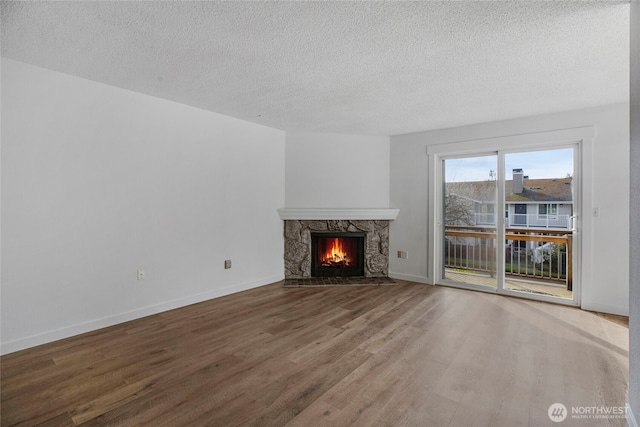 unfurnished living room with a textured ceiling, wood finished floors, baseboards, and a premium fireplace