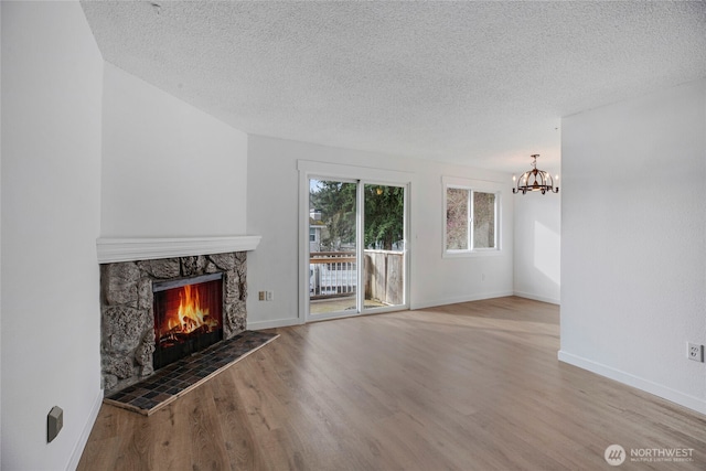 unfurnished living room with a stone fireplace, a notable chandelier, wood finished floors, and baseboards