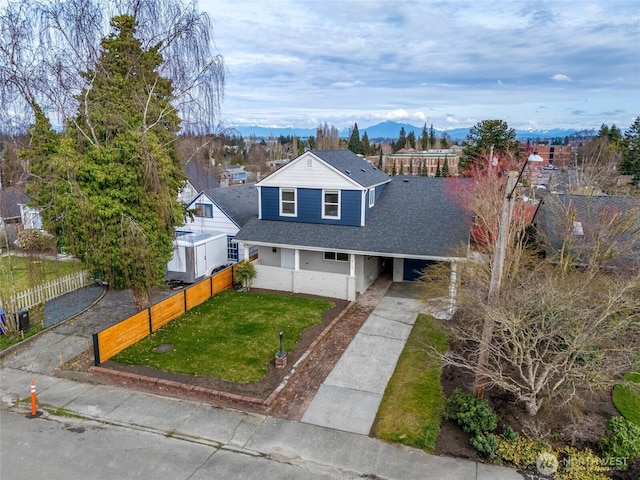 view of front of house with a front yard, fence, a shingled roof, concrete driveway, and a mountain view