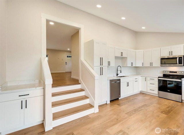 kitchen featuring light wood finished floors, lofted ceiling, a sink, light countertops, and appliances with stainless steel finishes