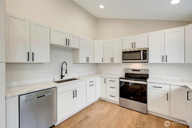 kitchen featuring a sink, lofted ceiling, light stone countertops, and stainless steel appliances