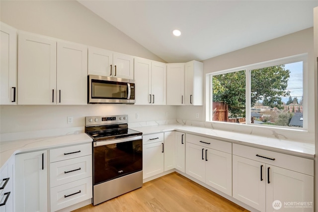 kitchen featuring light wood-style flooring, stainless steel appliances, white cabinets, light stone countertops, and vaulted ceiling