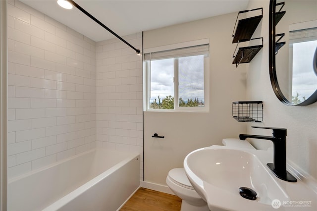 bathroom featuring washtub / shower combination, wood finished floors, baseboards, a sink, and toilet