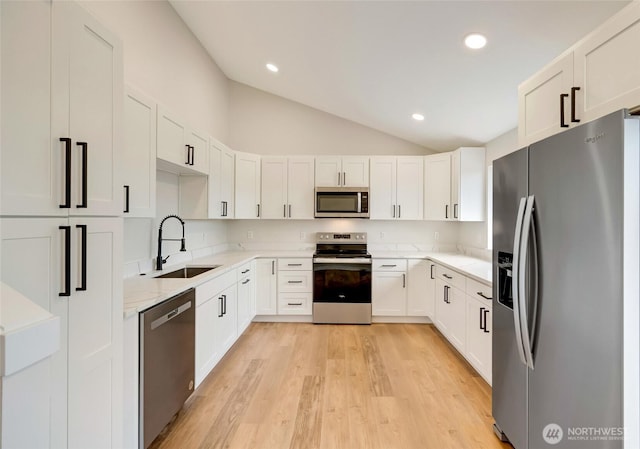 kitchen with light stone countertops, lofted ceiling, light wood-style floors, stainless steel appliances, and a sink