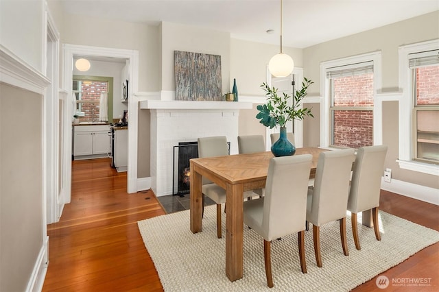 dining area featuring baseboards, dark wood-type flooring, and a brick fireplace