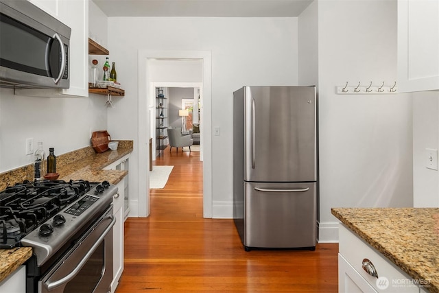 kitchen with white cabinets, light stone countertops, stainless steel appliances, and wood finished floors