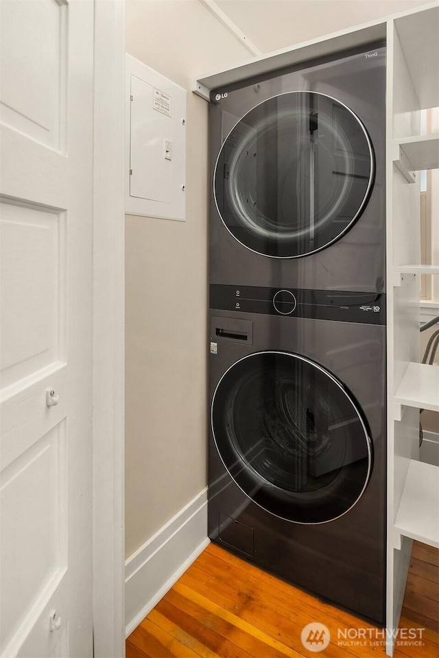 laundry area with stacked washer / drying machine, baseboards, wood finished floors, and laundry area