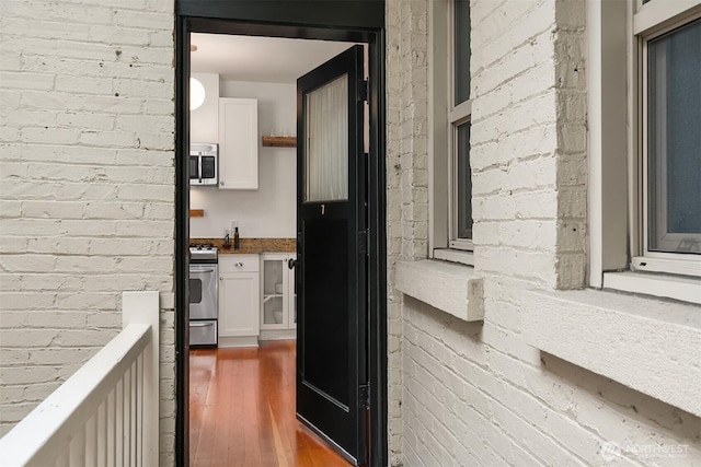 interior space with wood finished floors, appliances with stainless steel finishes, brick wall, and white cabinets