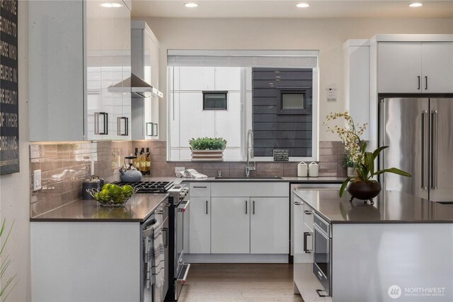 kitchen with dark countertops, tasteful backsplash, white cabinets, high end appliances, and a sink