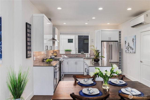 kitchen with dark countertops, high quality appliances, decorative backsplash, a wall mounted AC, and a sink