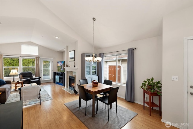 dining area featuring baseboards, light wood finished floors, a premium fireplace, lofted ceiling, and a chandelier