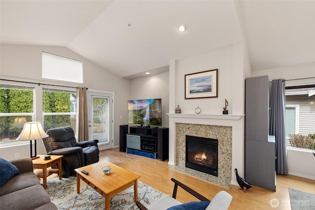 living area featuring baseboards, light wood finished floors, a premium fireplace, lofted ceiling, and recessed lighting