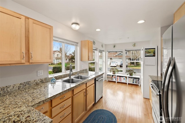 kitchen featuring light brown cabinets, light wood finished floors, stainless steel appliances, a sink, and tile counters