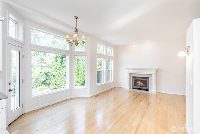 unfurnished living room with baseboards, a fireplace with flush hearth, a notable chandelier, and light wood-style flooring