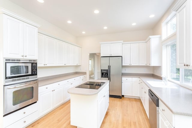 kitchen with a sink, a center island, light wood-style floors, appliances with stainless steel finishes, and white cabinets