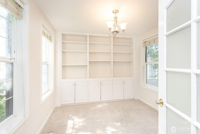 interior space with built in features, light colored carpet, baseboards, and a chandelier