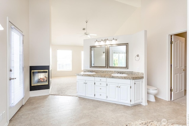 bathroom with a sink, a multi sided fireplace, toilet, and double vanity