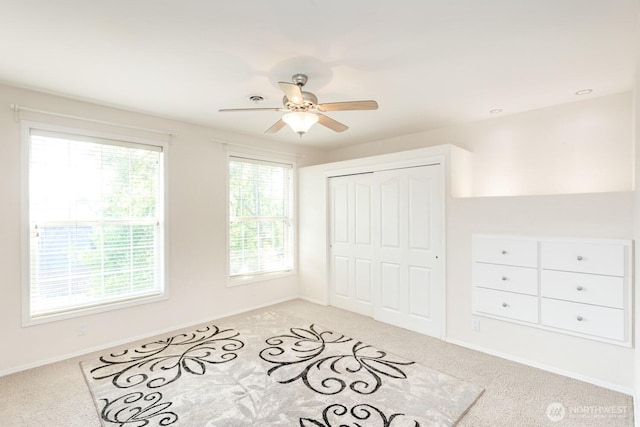 unfurnished bedroom featuring light carpet, baseboards, a closet, and a ceiling fan