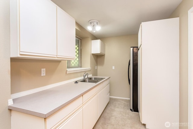 kitchen featuring light colored carpet, light countertops, white cabinets, refrigerator, and a sink