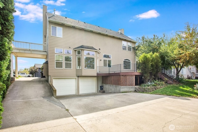 back of house featuring concrete driveway, stairway, an attached garage, and a chimney