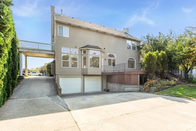 rear view of property featuring driveway, a chimney, stairs, and an attached garage