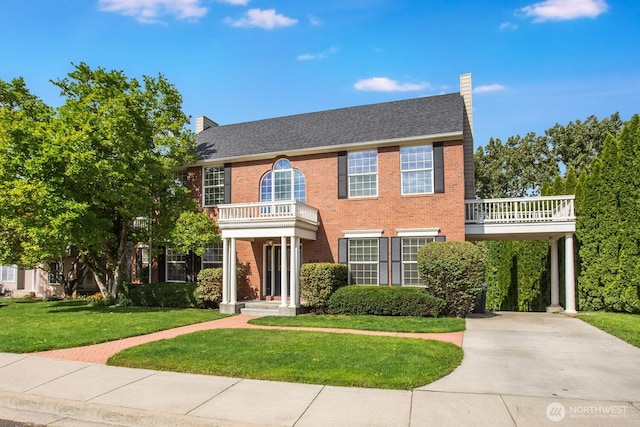 view of front facade with a front lawn, concrete driveway, brick siding, and a chimney