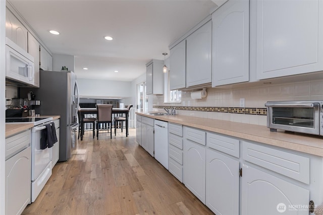 kitchen with white appliances, a toaster, light countertops, light wood-type flooring, and backsplash