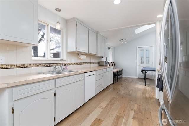 kitchen featuring light wood-type flooring, lofted ceiling with skylight, a sink, freestanding refrigerator, and white dishwasher