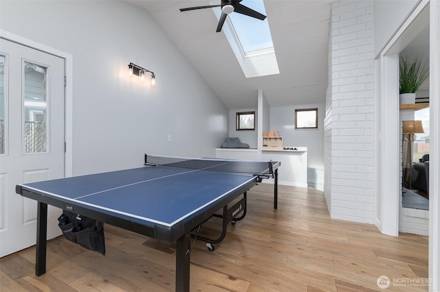 rec room with ceiling fan, vaulted ceiling with skylight, and light wood-style flooring