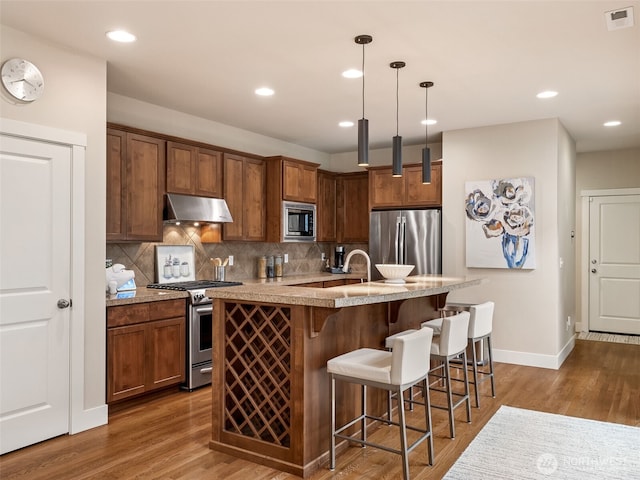 kitchen with visible vents, dark wood finished floors, stainless steel appliances, decorative backsplash, and under cabinet range hood