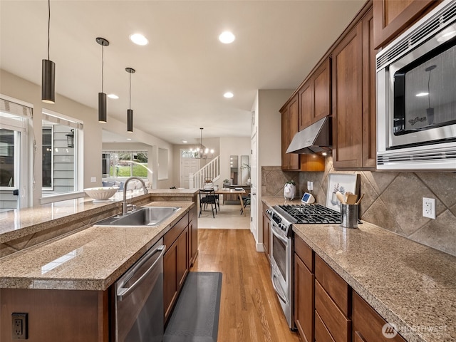 kitchen with light wood-type flooring, under cabinet range hood, a sink, backsplash, and stainless steel appliances