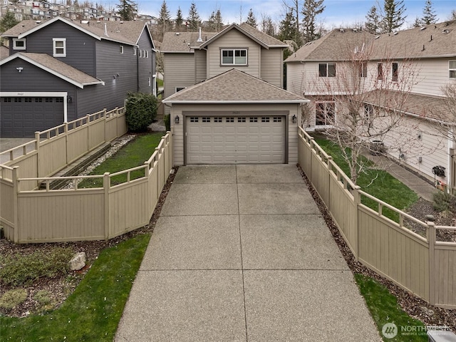 view of front of house with an attached garage, concrete driveway, fence, and a shingled roof