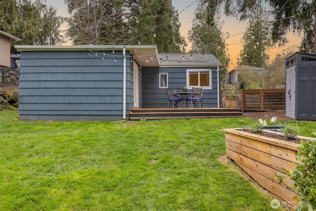 back of house at dusk featuring a deck, a yard, and fence