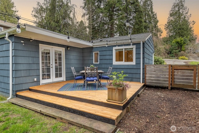 deck at dusk with outdoor dining space, french doors, and fence