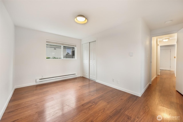 empty room with a baseboard heating unit, baseboards, and wood finished floors