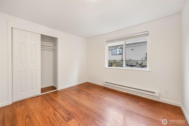 unfurnished bedroom featuring a baseboard heating unit, wood finished floors, a closet, and baseboards