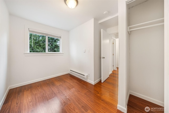 unfurnished bedroom featuring wood finished floors, baseboards, and a baseboard radiator