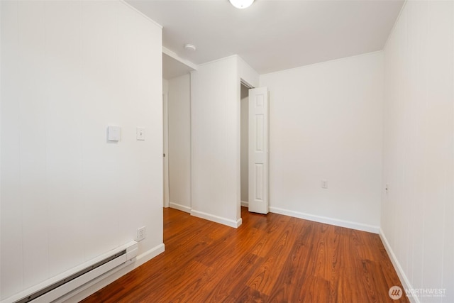 spare room featuring a baseboard radiator, baseboards, and wood finished floors