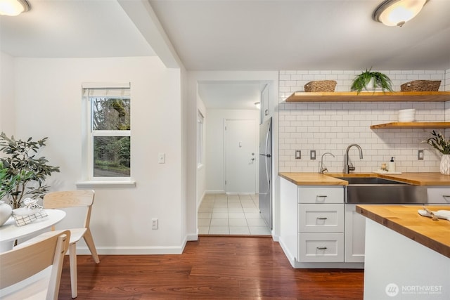 kitchen featuring freestanding refrigerator, backsplash, wooden counters, and a sink