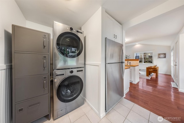 washroom featuring a wainscoted wall, laundry area, light tile patterned flooring, and stacked washer / drying machine