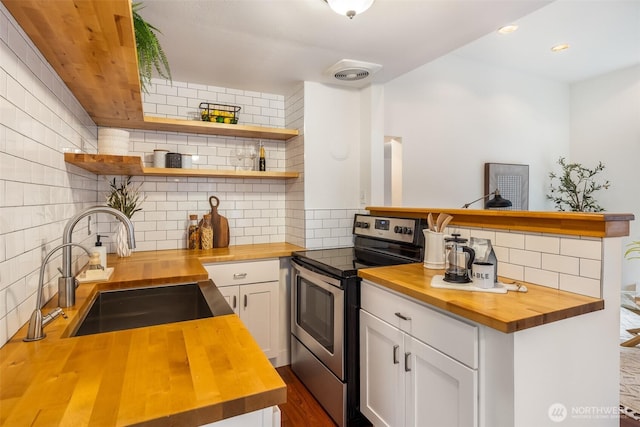 kitchen featuring stainless steel electric range, a sink, butcher block countertops, white cabinetry, and backsplash