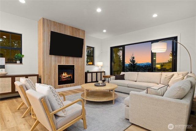 living area with recessed lighting, a lit fireplace, and wood finished floors