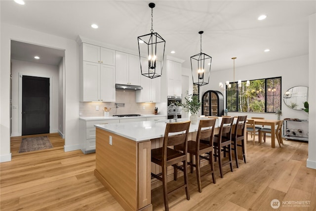 kitchen featuring gas cooktop, light wood finished floors, light countertops, and under cabinet range hood